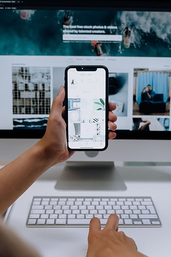 Person uses a smart in front of a computer screen displaying stock , showcasing modern technology use. HD phone wallpaper