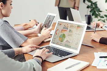 Coworkers analyzing data charts on laptops during a team meeting. HD wallpaper