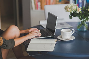 Female lancer using laptop with coffee at home office desk, surrounded by roses and a planner. HD wallpaper