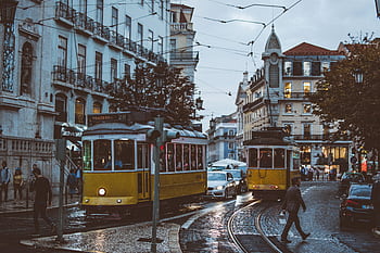 Scenic view of trams navigating the charming streets of Lisbon at dusk, capturing urban life and transportation. HD wallpaper