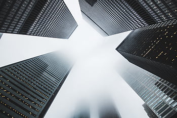 Misty city scene with towering skyscrapers disappearing into the fog, creating a moody urban environment. HD wallpaper