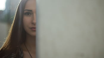A mysterious and captivating portrait of a young woman partially hidden behind a soft focus background. HD wallpaper