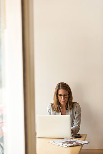 Businesswoman working remotely on a laptop at home, enjoying natural light in a modern, minimalist setting. HD phone wallpaper