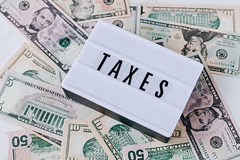 US dollar bills surrounding a sign showing 'TAXES'. Ideal for financial context. HD wallpaper