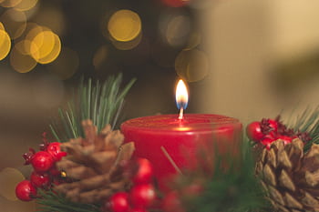 Red candle with pine cones and blurred bokeh lights, perfect for holiday decor inspiration. HD wallpaper