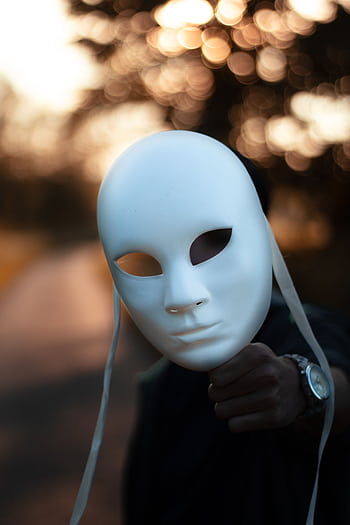 A person holds a white mask, creating a mysterious and conceptual portrait with bokeh background. HD phone wallpaper