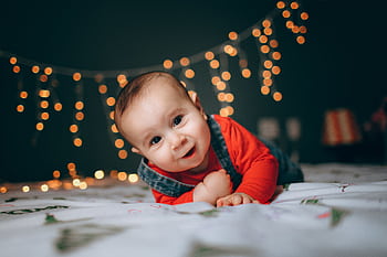 Cute baby boy lying on bed with festive string lights creating a warm, cozy atmosphere. HD wallpaper