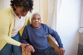 A woman assists an elderly man indoors, focusing on care and support. HD wallpaper
