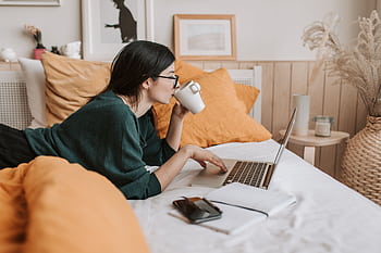 Woman relaxing on bed with coffee browsing laptop for lance work or online learning. HD wallpaper