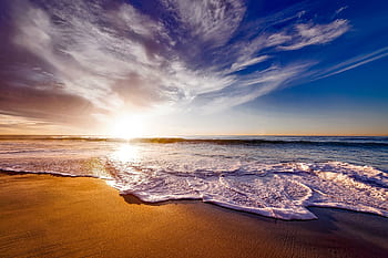 Breathtaking sunset over the ocean with gentle waves lapping on a sandy beach, creating a peaceful and serene atmosphere. HD wallpaper