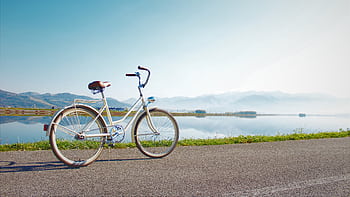 A vintage bicycle on a lakeside road with mountain views under a clear sky. HD wallpaper