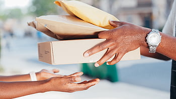 Close-up of hands exchanging packages outdoors. Represents delivery and shipping services. HD wallpaper