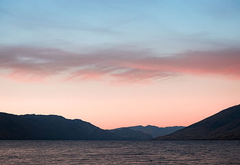 A serene landscape featuring a pastel sunset above a calm lake, framed by distant mountains. HD wallpaper