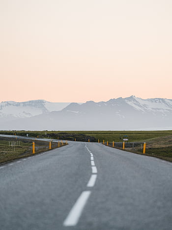 A stunning view of an empty Icelandic road leading towards majestic mountains at sunset, perfect for travel and adventure themes. HD phone wallpaper