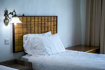 A stylish bedroom featuring a wooden headboard, wall lamp, and white bedding. HD wallpaper