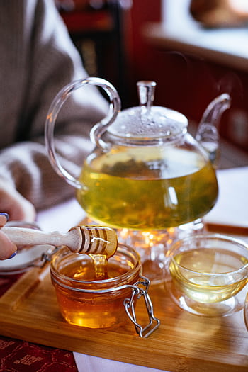 A warm and inviting scene featuring a glass teapot with tea and a jar of honey on a wooden tray. HD phone wallpaper