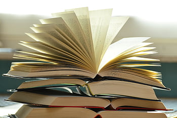 A close-up of a stack of open books with pages fanned out, capturing a study atmosphere. HD wallpaper