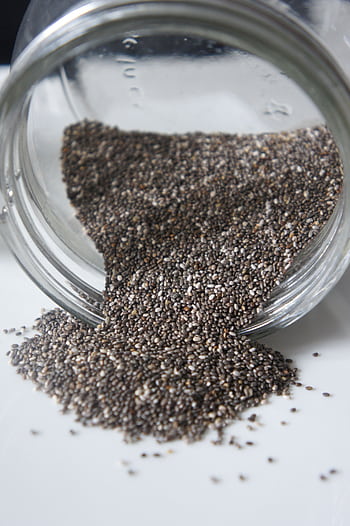 Chia seeds pouring out from a glass jar, perfect for healthy lifestyle or food blogs. HD phone wallpaper