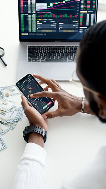 A person trading stocks using a smart, showcasing financial data on mobile and laptop screens. HD phone wallpaper
