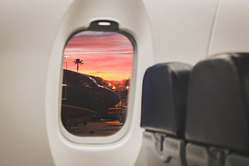 Scenic sunset view through airplane window with plane and palm silhouettes on tarmac. HD wallpaper