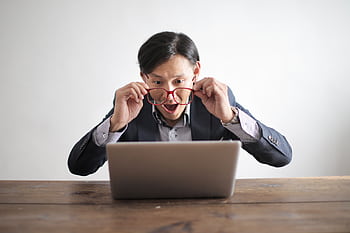 Surprised man in a suit looking at laptop, expressing disbelief indoors. HD wallpaper
