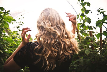 Blonde woman with curly hair surrounded by lush greenery, enjoying a sunny day. HD wallpaper