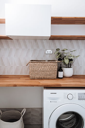 Bright and tidy laundry room featuring a washing machine, wicker basket, and potted plant on a wooden counter. HD phone wallpaper