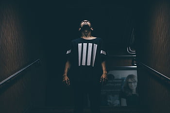 A young man stands in a dimly lit subway, looking upwards with a dramatic pose. HD wallpaper
