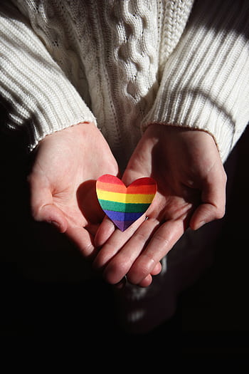 Close-up of hands cradling a rainbow heart, symbolizing love and LGBTQ+ pride. HD phone wallpaper