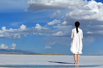 Woman stands alone on a vast salt flat under a bright blue sky with clouds. HD wallpaper