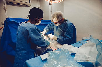 Surgeons focusing on a procedure in an equipped operating room, showcasing teamwork and precision. HD wallpaper