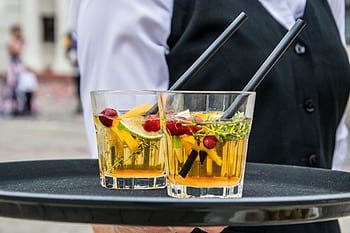 Delicious orange cocktails with cranberries and herbs on a tray, served by waiter at an outdoor event. HD wallpaper