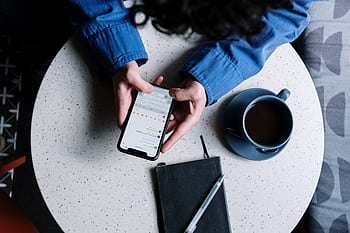 Person using smart at table with notebook and coffee, ideal for tech and lifestyle themes. HD wallpaper
