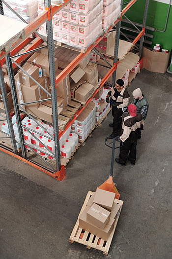 Three warehouse workers discussing inventory organization details. HD phone wallpaper