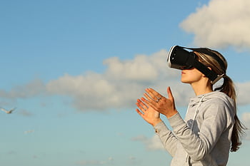 Woman using VR headset outdoors, exploring virtual reality under a clear blue sky. HD wallpaper