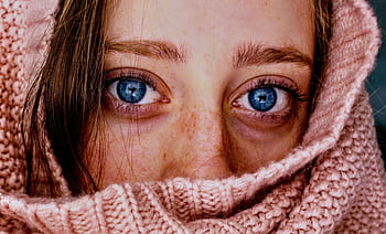 Intense close-up of a woman's blue eyes wrapped in a soft, pink knit scarf. HD wallpaper