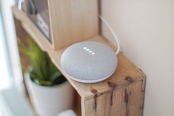 A Google Home Mini smart speaker on a wooden shelf, blending technology with home decor. HD wallpaper