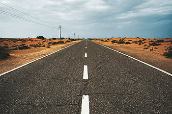 Straight, empty desert road under cloudy sky in Dubai, UAE, highlighting solitude and vastness. HD wallpaper