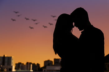 Silhouette of a couple embracing at sunset in an urban setting, evoking romance. HD wallpaper