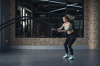 Focused woman performing CrossFit rope training indoors, demonstrating strength and endurance. HD wallpaper