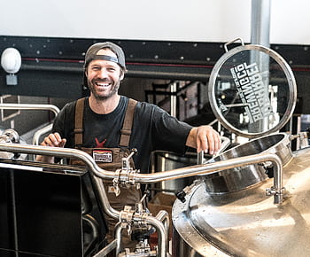 Happy brewer in a craft brewery standing near stainless steel equipment. HD wallpaper