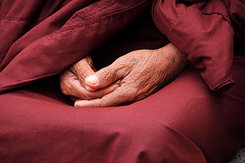 Close-up of a monk's hands in prayer, wrapped in maroon robe, symbolizing peace and spirituality. HD wallpaper
