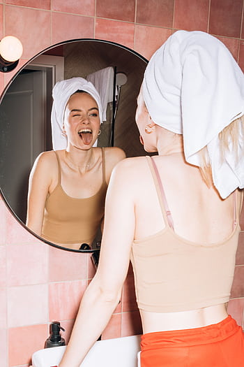 A young woman with a towel on her head makes a funny expression in a bathroom mirror. HD phone wallpaper