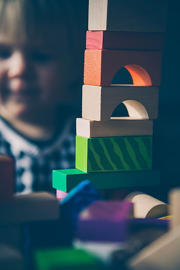 A child plays with colorful wooden blocks, building creative structures. HD phone wallpaper
