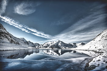 A breathtaking view of a snowy mountain lake reflecting the sky, with serene winter scenery. HD wallpaper