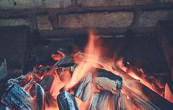 Warm glowing embers and flames from firewood in a rustic fireplace setting. HD wallpaper