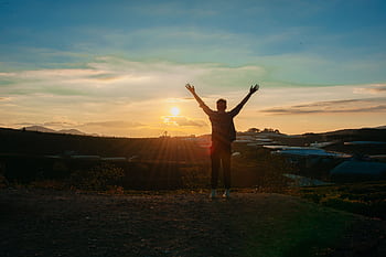 Man raises arms in dom at sunset, embracing the vastness of nature's beauty. HD wallpaper
