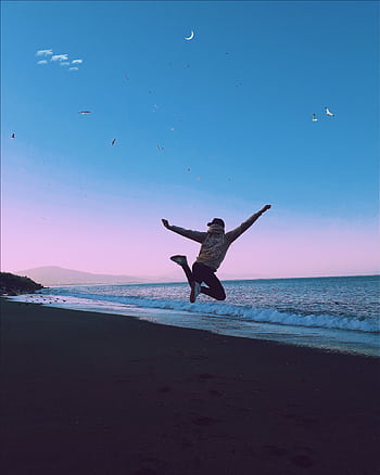 A man jumping on a beach under a crescent moon, symbolizing dom and joy. HD phone wallpaper