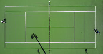 High-angle drone shot of a tennis match on a bright green court with shadows. HD wallpaper