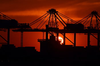 Silhouette of cargo cranes against a vivid sunset at an industrial container port. HD wallpaper